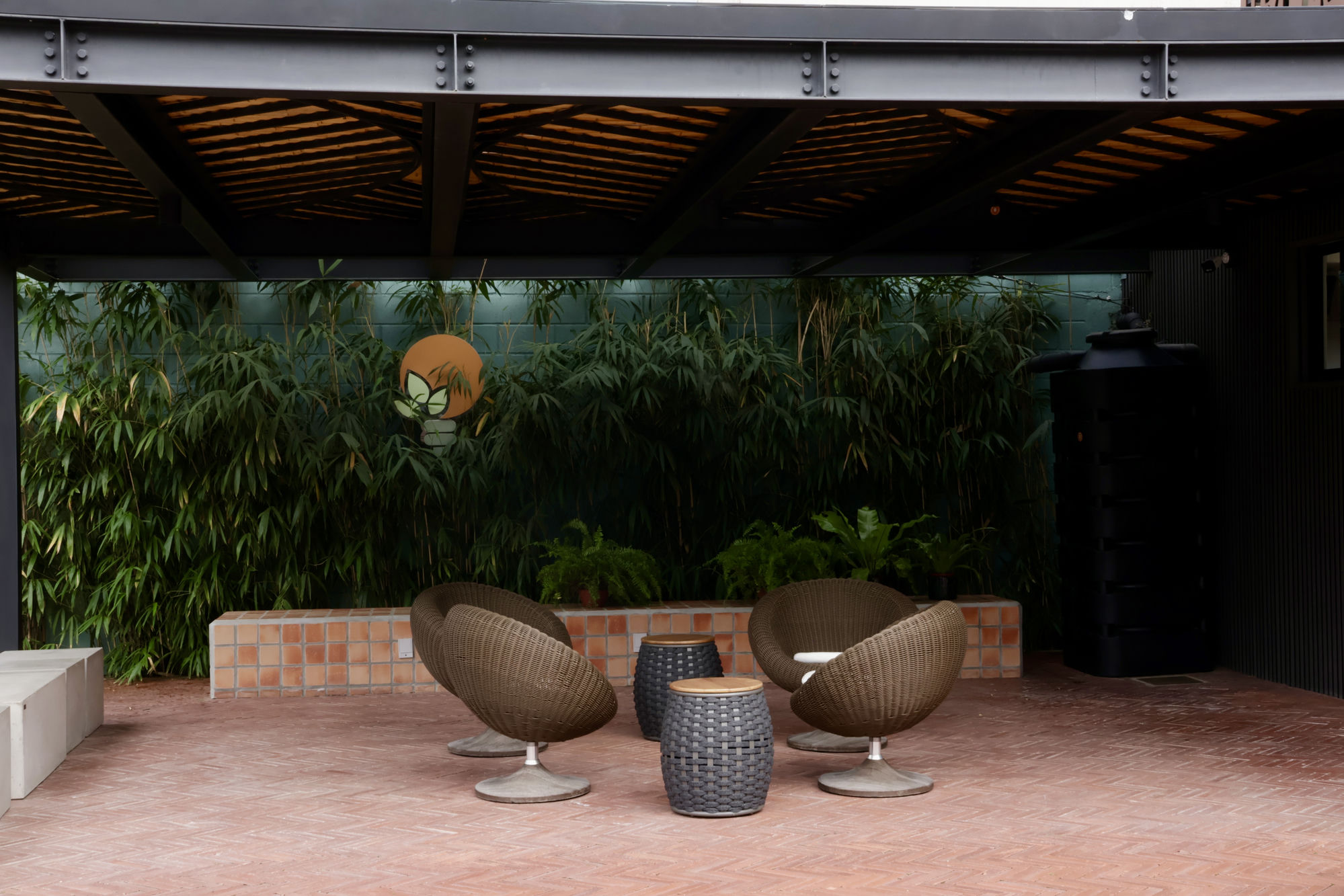 Área de estar da Galeria Panaceia com poltronas, bambu e o símbolo da marca na parede